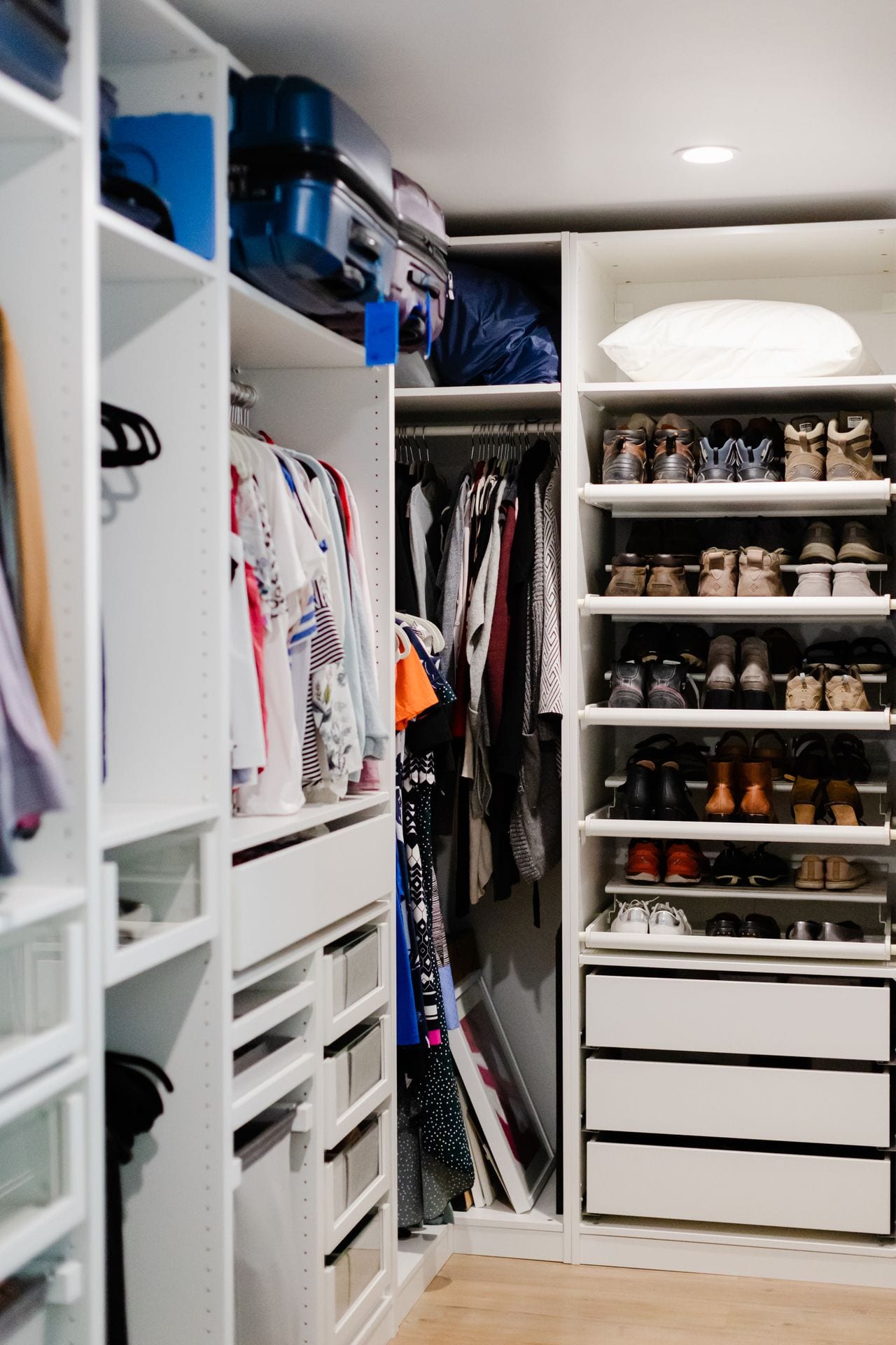Organized walk-in closet with clothing, luggage, drawers, and dedicated shoe storage